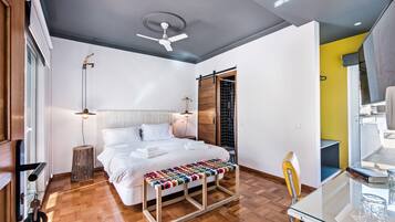 Ein modernes Schlafzimmer mit einem Bett, einem Nachttisch, einer Lampe und einer Bank mit farbigem Kissen.