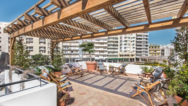 Una terraza en la azotea con pérgola de madera, plantas en macetas y sillones de descanso.