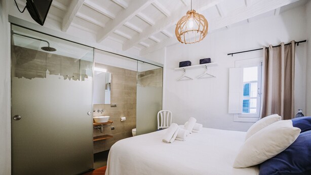 A hotel room with a bed, a bathroom, and a glass door leading to a shower area.