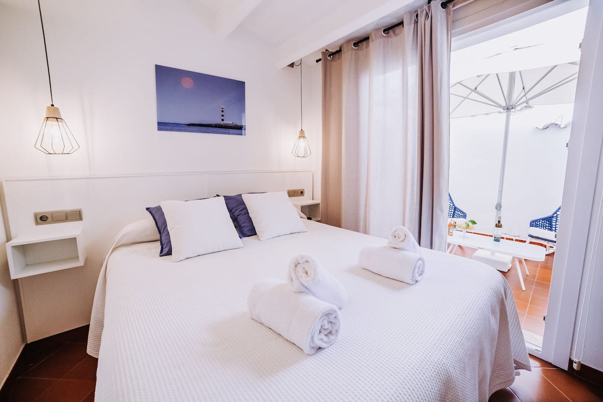 Habitación de hotel con una cama grande, una mesita de noche, un estante en la pared y vistas al balcón.