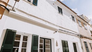 A white building with green shutters, a tiled roof, and a cobblestone street.