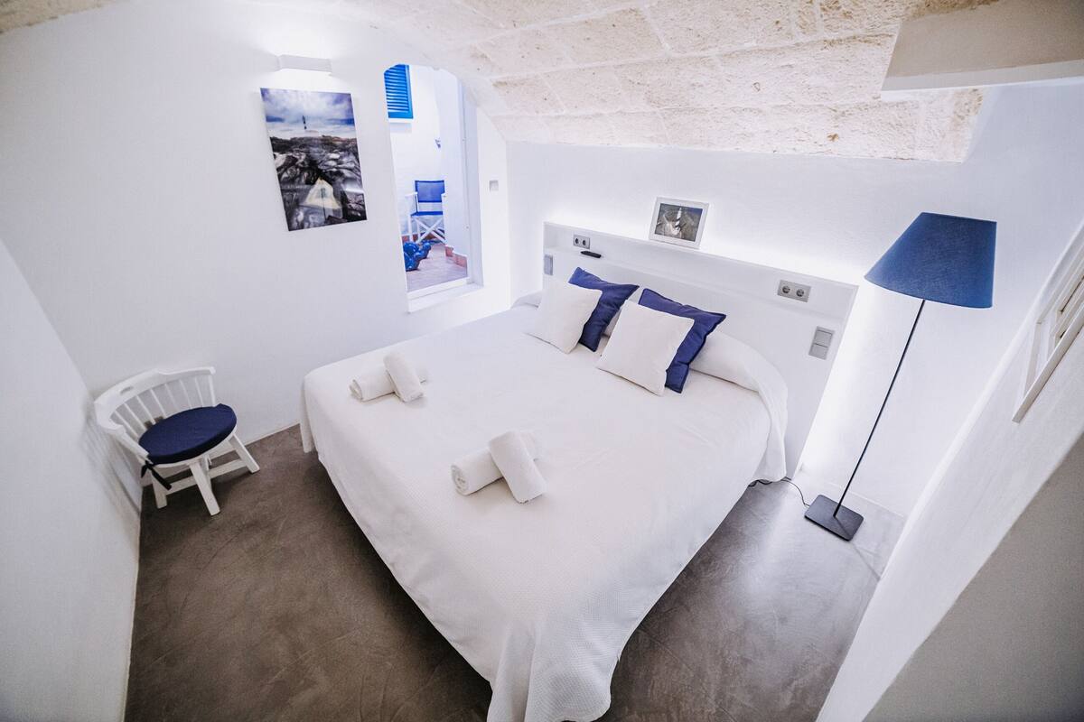 Un dormitorio con una cama grande, una silla, un escritorio y una lámpara.