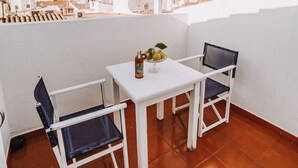 A rooftop terrace with a white table and two chairs, a bottle of wine, and a bowl of fruit.
