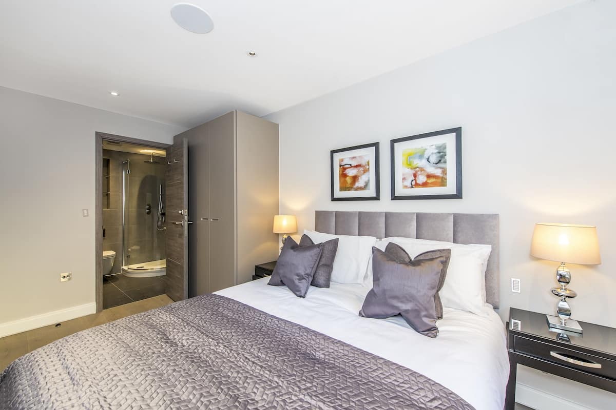 Ein modernes Hotelzimmer mit einem großen Bett, einer Duschkabine aus Glas und zwei gerahmten Kunstwerken an der Wand.