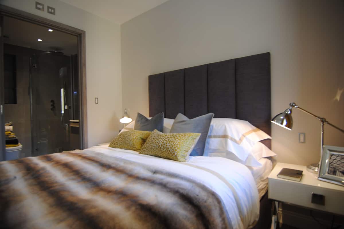 Ein modernes Hotelzimmer mit einem großen Bett, einem Nachttisch mit Lampe und einer Tür zum Badezimmer.