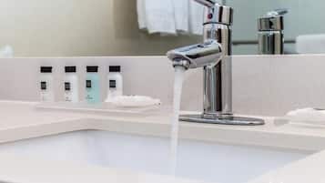 Un baño moderno con grifo cromado, lavamanos blanco y una fila de artículos de aseo en la encimera.
