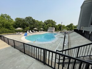A swimming pool with lounge chairs and umbrellas, surrounded by a fence and trees.