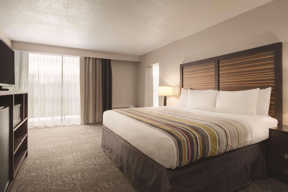 Una habitación de hotel con una cama grande, televisión, escritorio y ventana con cortinas.