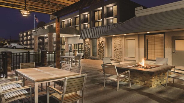 An outdoor patio area with tables and chairs, a fire pit, and a building with multiple balconies.
