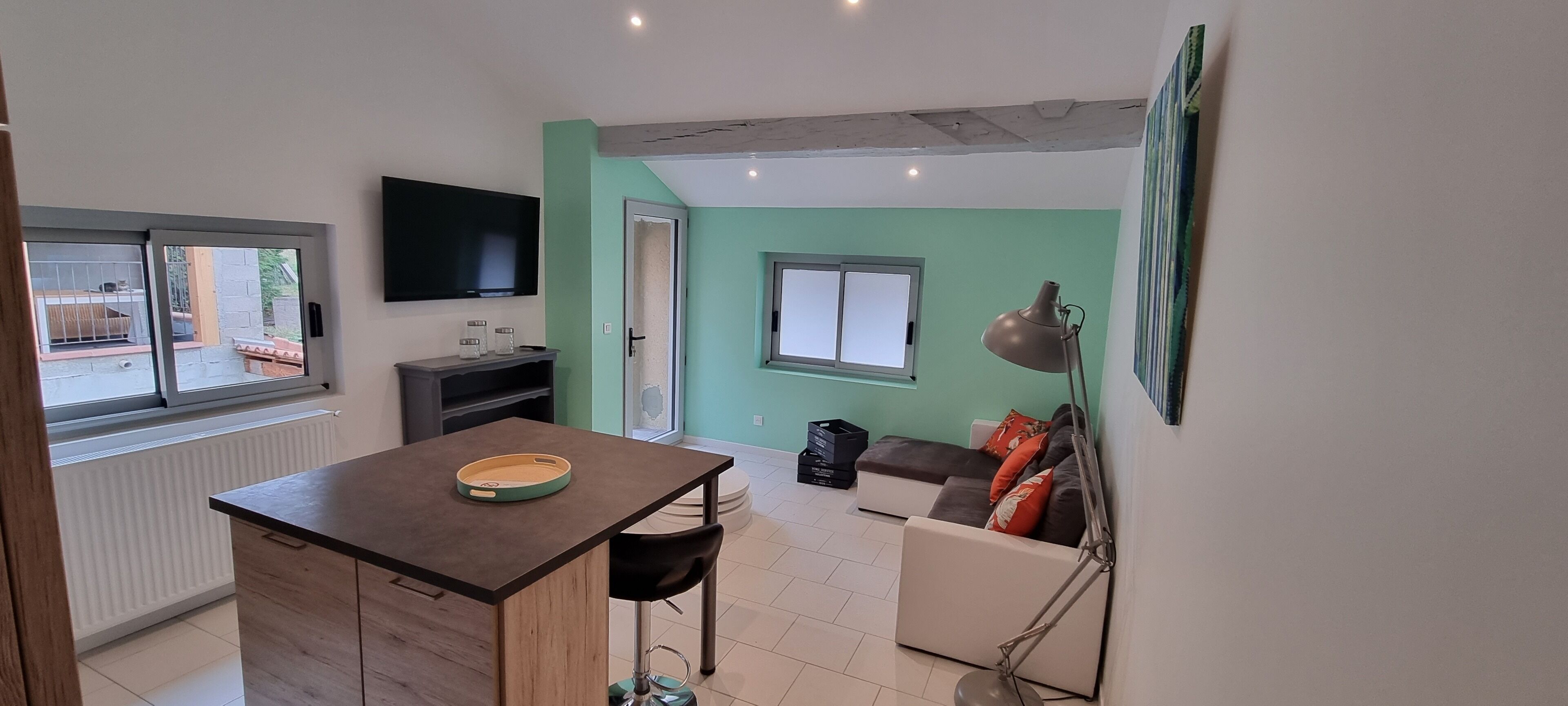 A compact living space with a kitchen area, a dining table, a sofa, and a TV mounted on the wall.