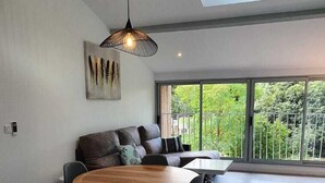 Un comedor amplio con una mesa redonda y sillas, una lámpara colgante moderna, y vistas a zonas verdes a través de grandes ventanales.