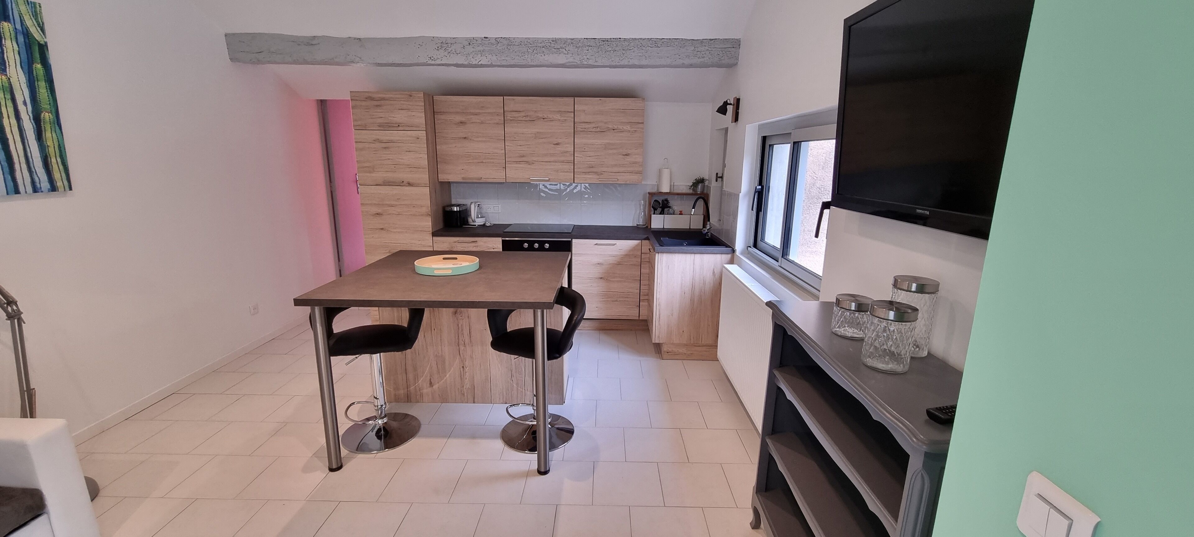 A compact kitchen with wooden cabinets, a black countertop, and a dining table with two chairs.
