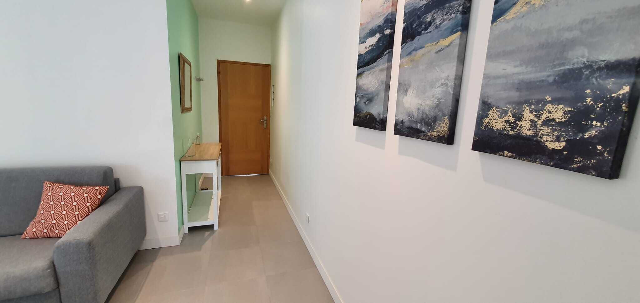 Un pasillo con un sofá gris, una mesita blanca y dos cuadros abstractos en la pared.