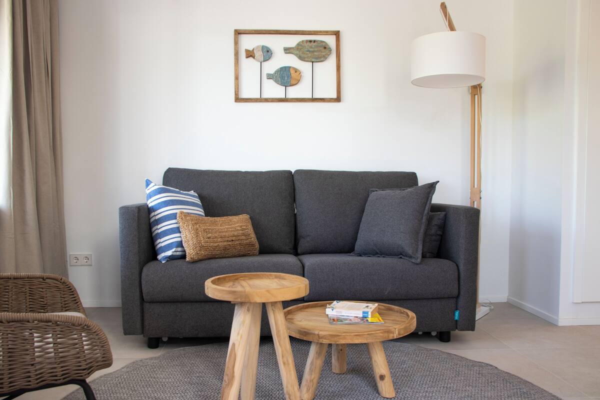 A modern living room with a grey sofa, a wooden side table, a wicker chair, and a floor lamp.
