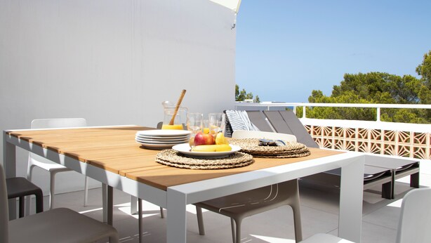 Een eetgedeelte met een houten tafel, witte stoelen en een witte parasol.