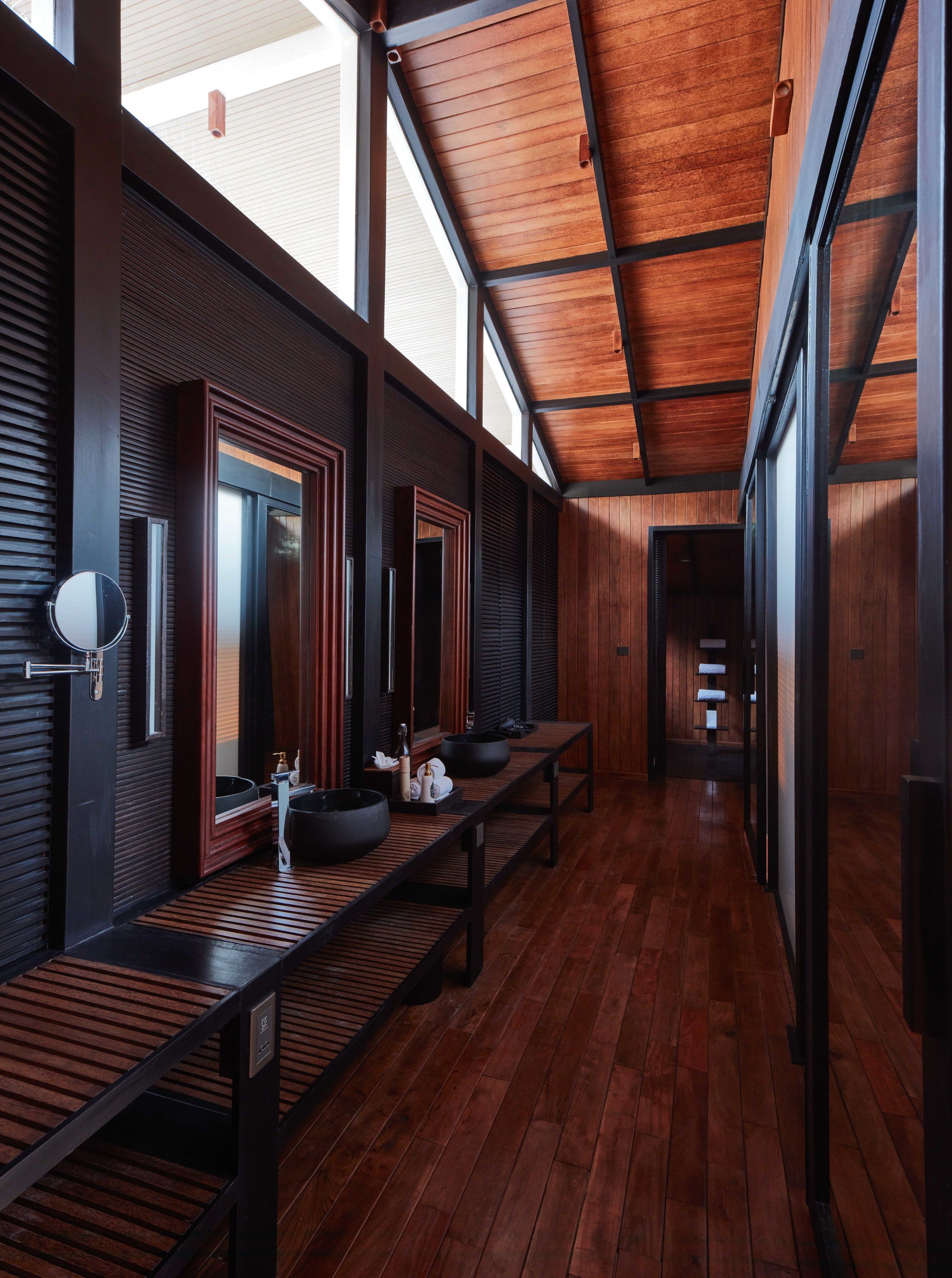 A modern bathroom with wooden floors, large mirrors, and a skylight.