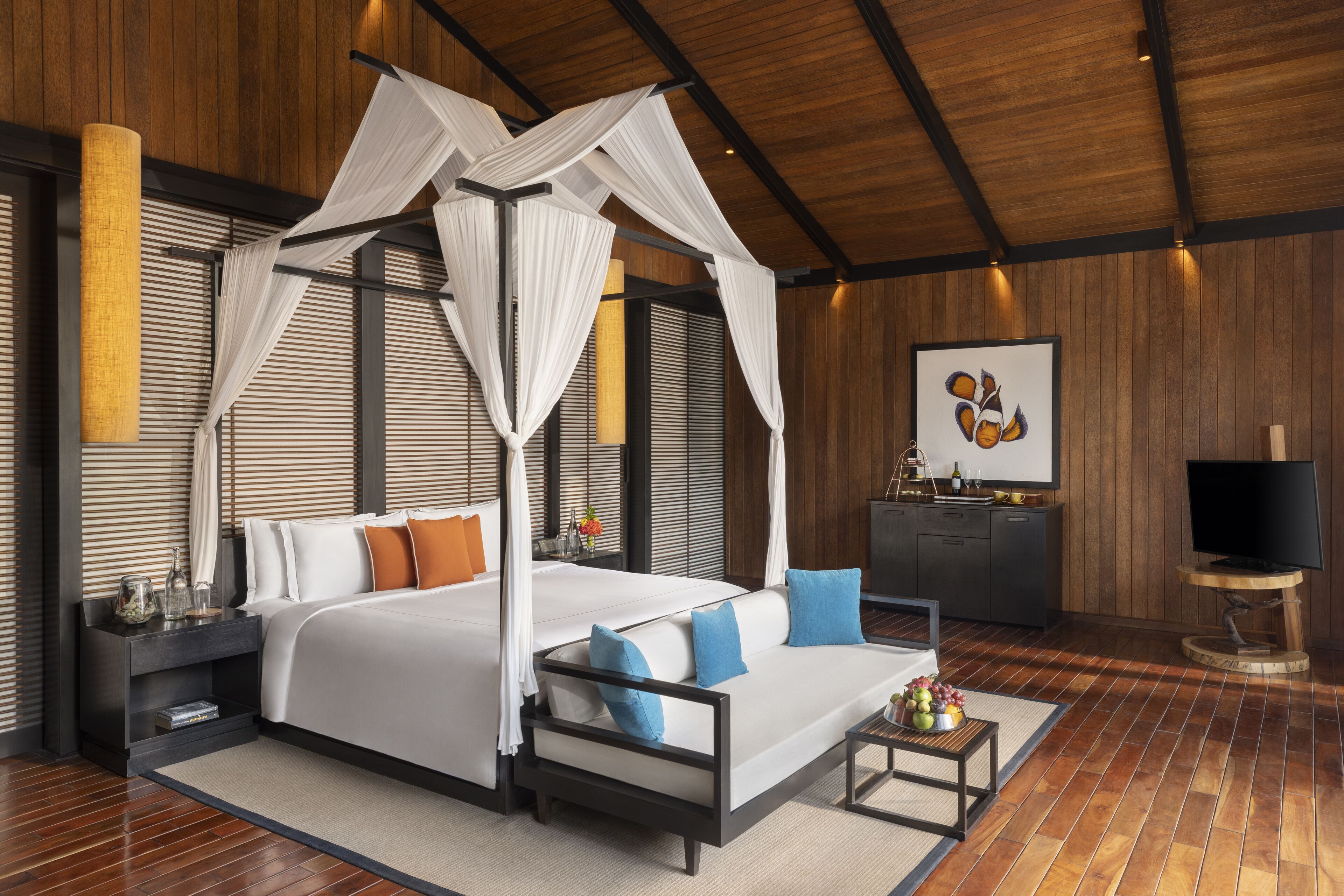 A modern bedroom with a canopy bed, a sofa, a TV, and a minibar.