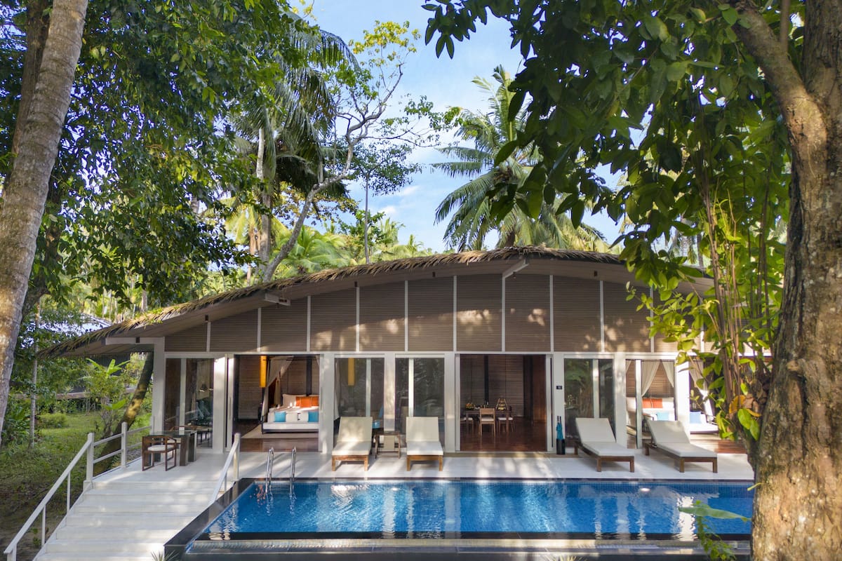 A modern villa with a swimming pool, outdoor seating, and a thatched roof.