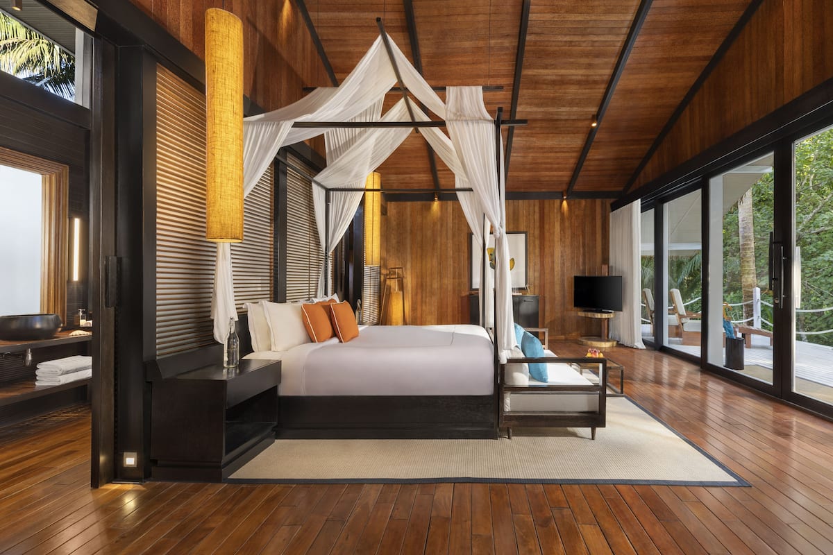 A spacious bedroom with a large bed, a bedside table, a TV, and a view of the outdoors.