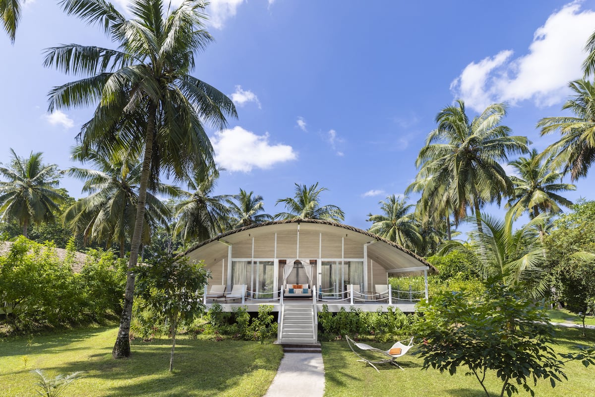A resort with a covered lounge area, palm trees, and a clear sky.