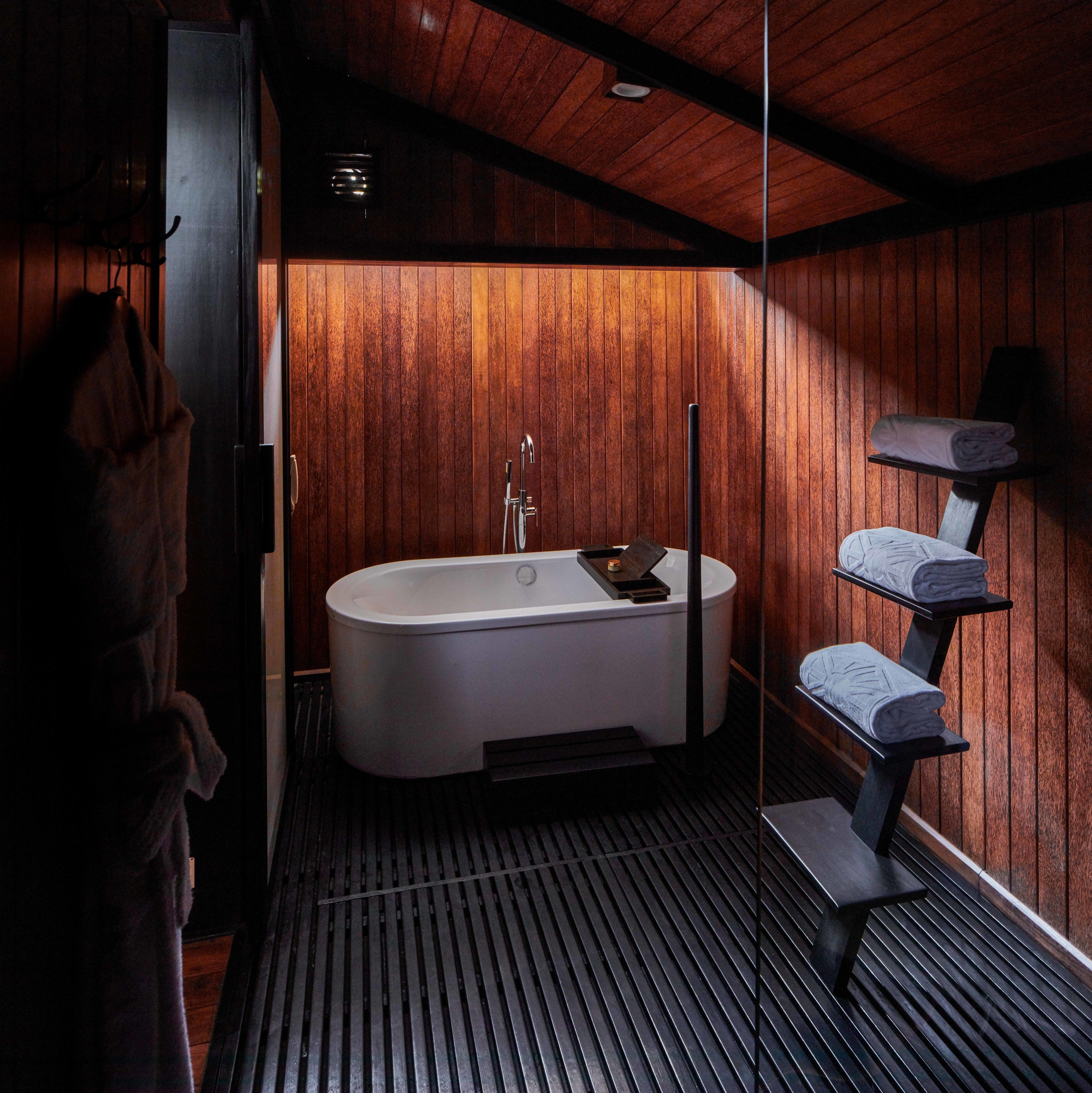 A modern bathroom with a freestanding bathtub, wooden panel walls, and a bench with towels.