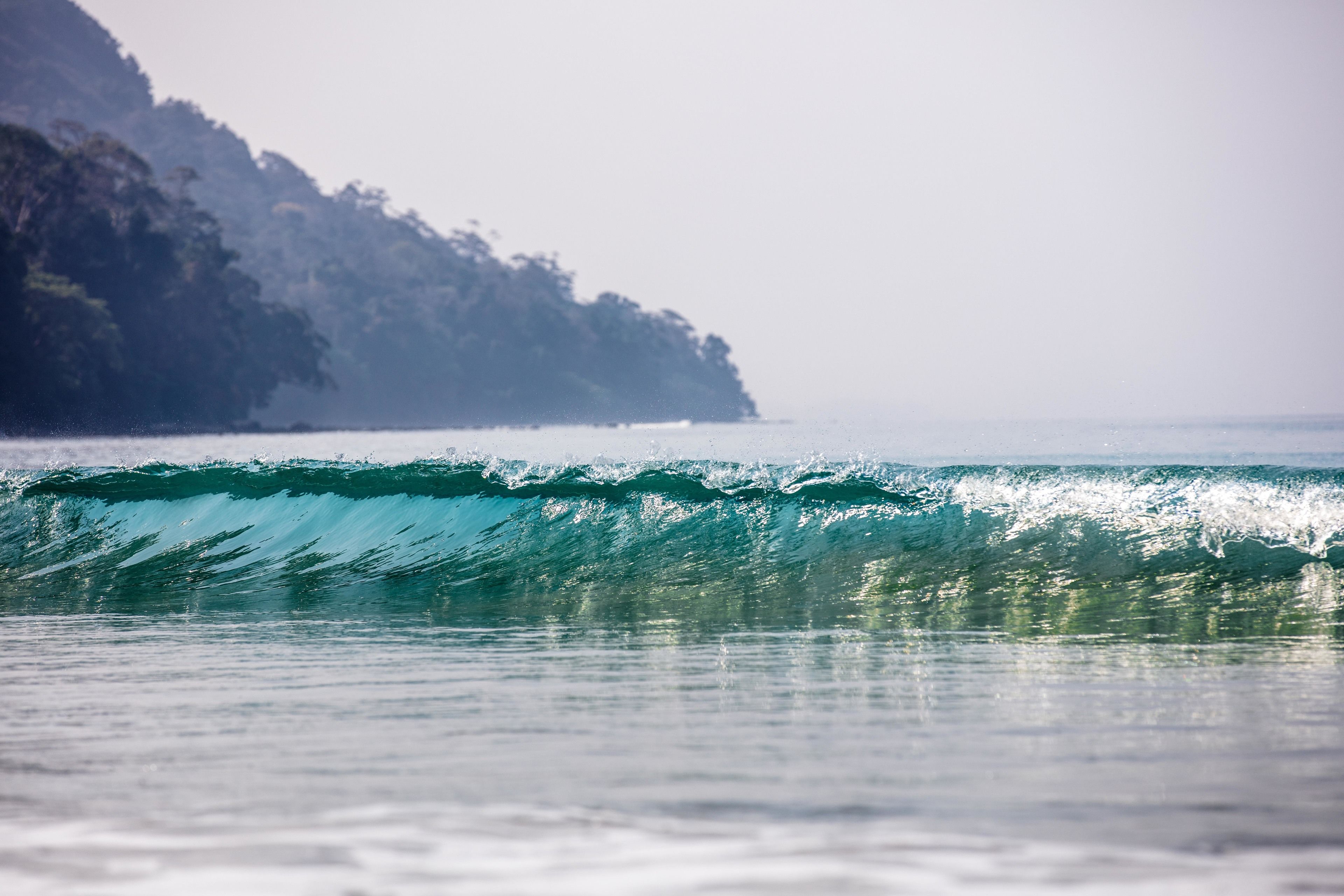 A wave in the ocean with a rocky coastline in the background.