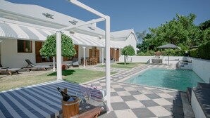 Zona de piscina con suelo a cuadros, sillones de descanso y un área de estar cubierta.