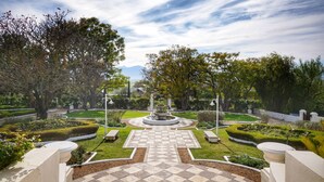 Un jardín ajardinado con una fuente central, senderos y setos bien cuidados.