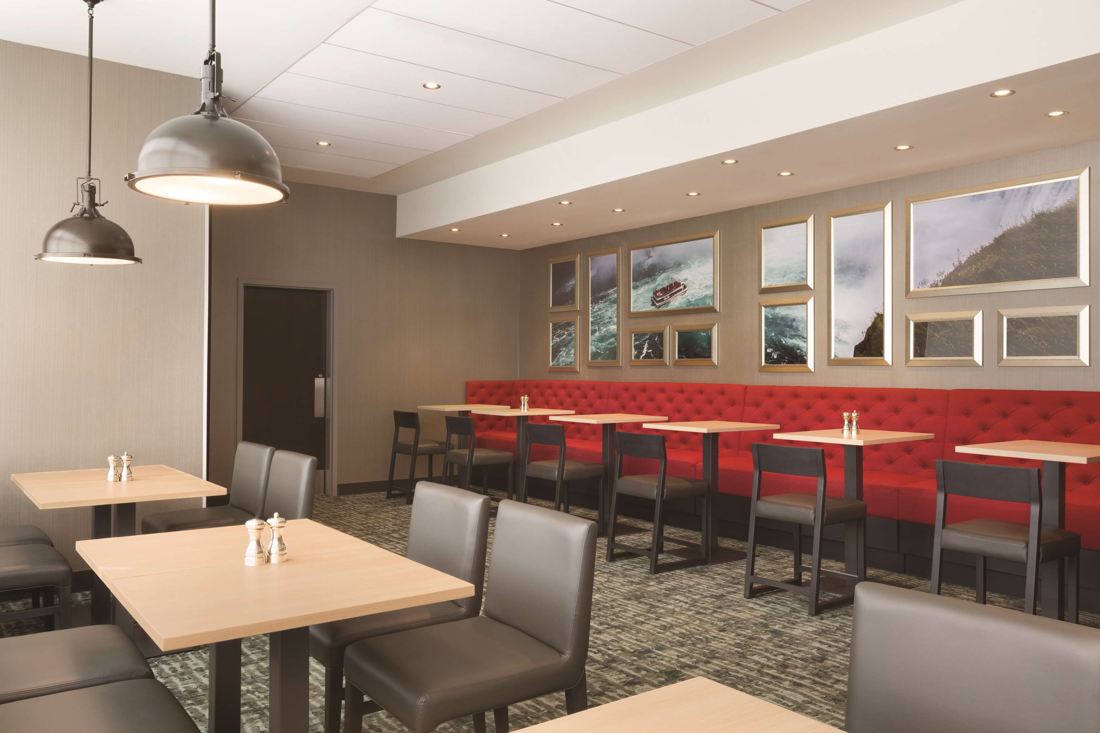 Un restaurante con cabinas y mesas, un banco acolchado rojo y cuadros en la pared.