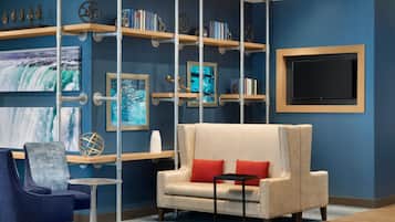 A modern living room with a beige sofa, red cushions, a blue armchair, a small round table, and a bookshelf with decorative items and books.