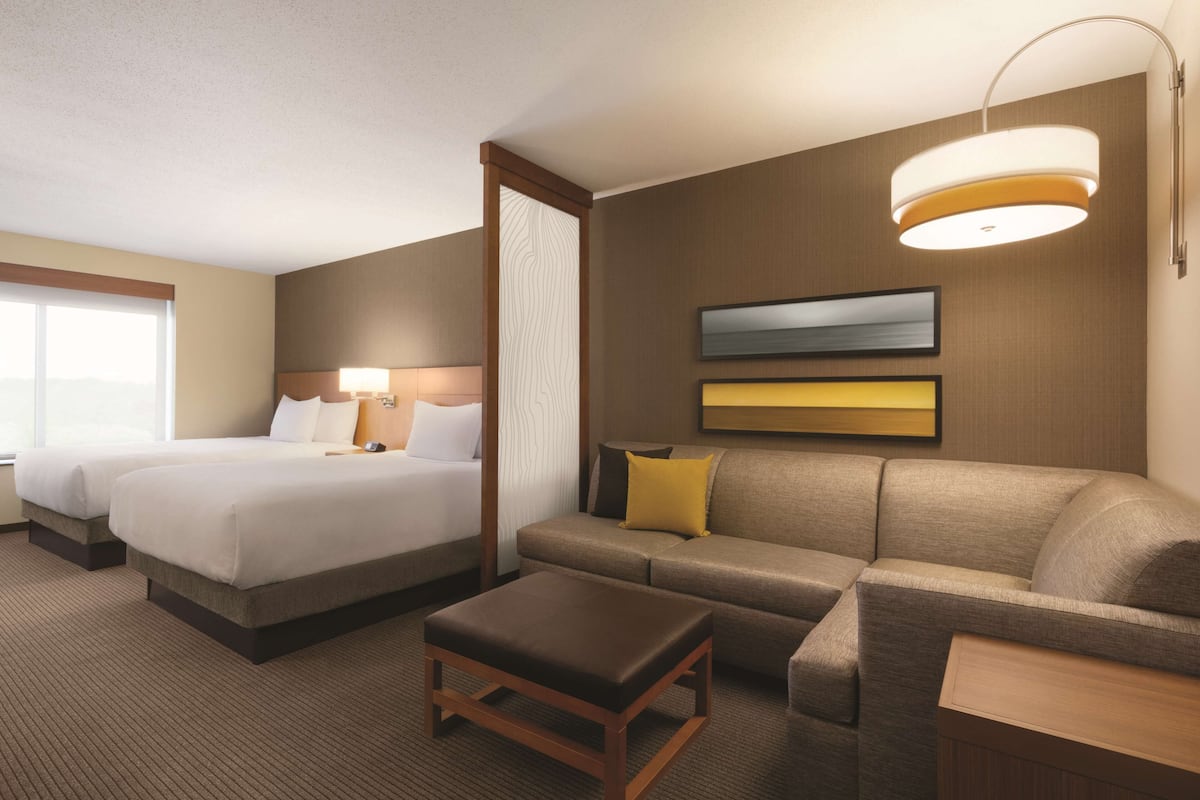 Ein Hotelzimmer mit zwei Betten, einer Couch, einem kleinen Tisch und einer Lampe.