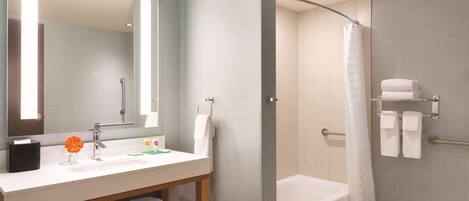 A modern bathroom with a white sink, mirror, and bathtub. There are towels and a shower curtain visible.