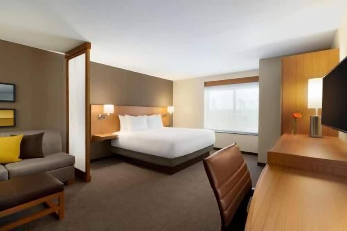 Ein Hotelzimmer mit Bett, Schreibtisch, Stuhl, Sofa und Fernseher.