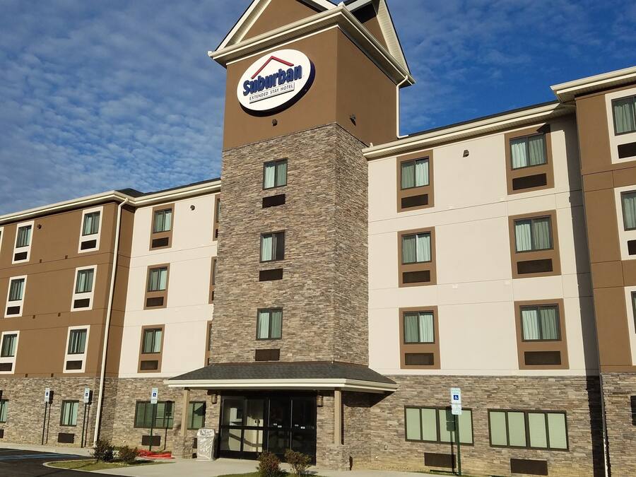 A Suburban Extended Stay Hotel with a prominent sign, multiple floors, and a parking lot with handicapped spaces.