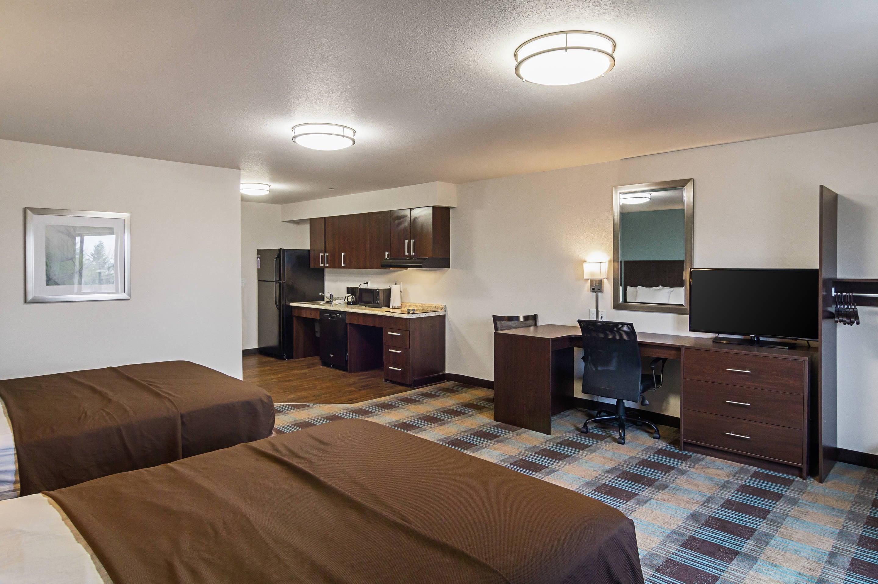 Une chambre d’hôtel avec deux lits, une kitchenette, un bureau avec une chaise, une télévision et un miroir.
