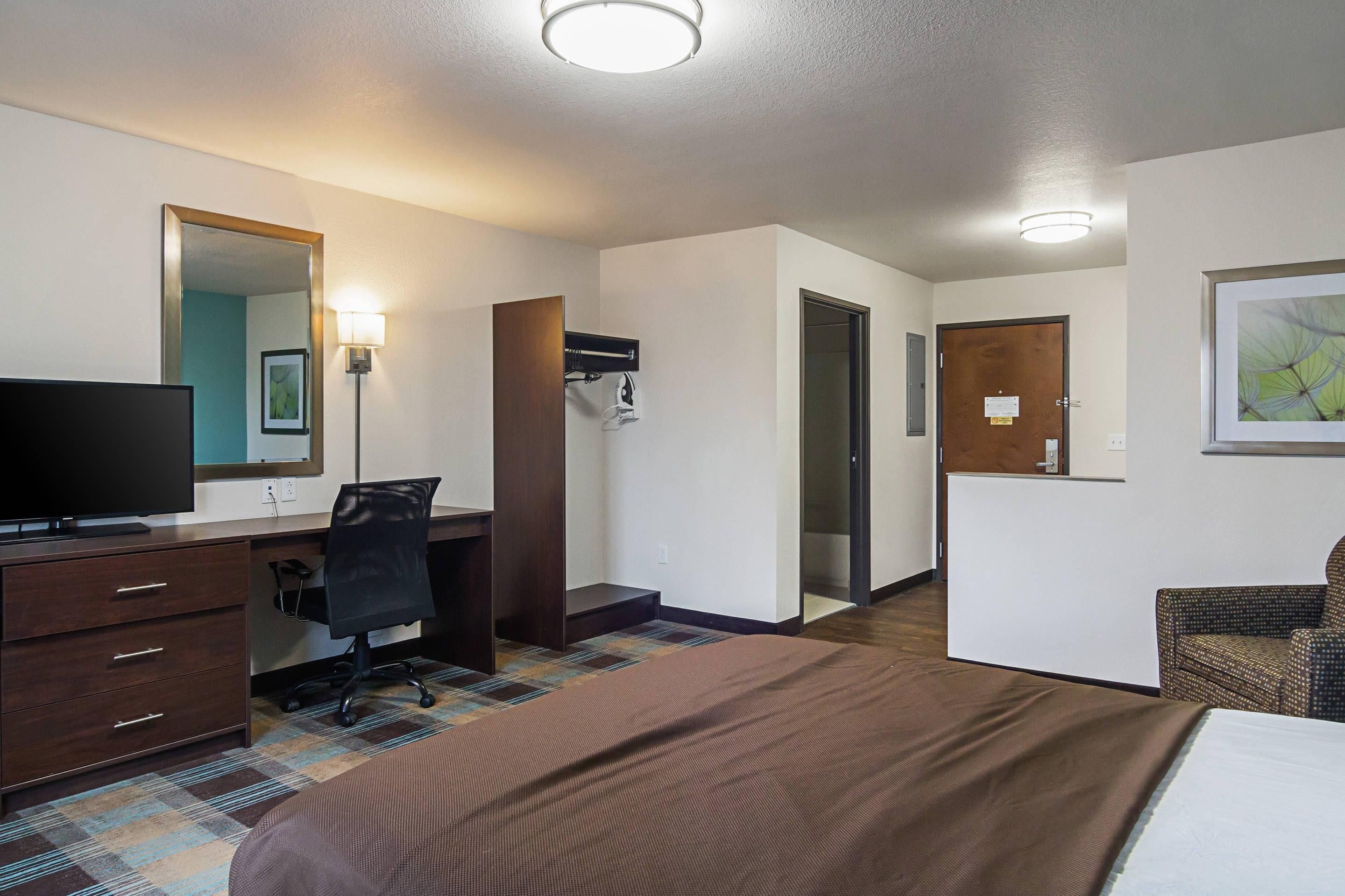 Una habitación de hotel con cama, escritorio y silla, televisor, espejo y puerta que da a otra habitación.