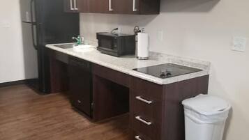 A compact kitchen with dark wooden cabinets, a black refrigerator, a microwave, and a trash bin.
