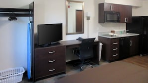 A compact hotel room with a dark wood desk, a flat-screen TV, a microwave, a refrigerator, and a small kitchenette. - Suburban Studios Monaca - Pittsburgh (Monaca)