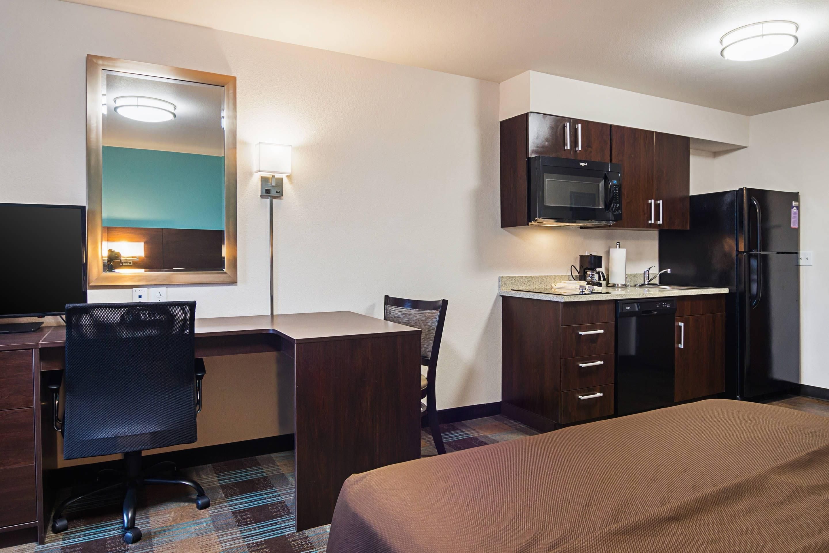 Une chambre d’hôtel équipée d’un lit, d’un bureau, d’une chaise, d’un four à micro-ondes, d’un réfrigérateur et d’une petite kitchenette.