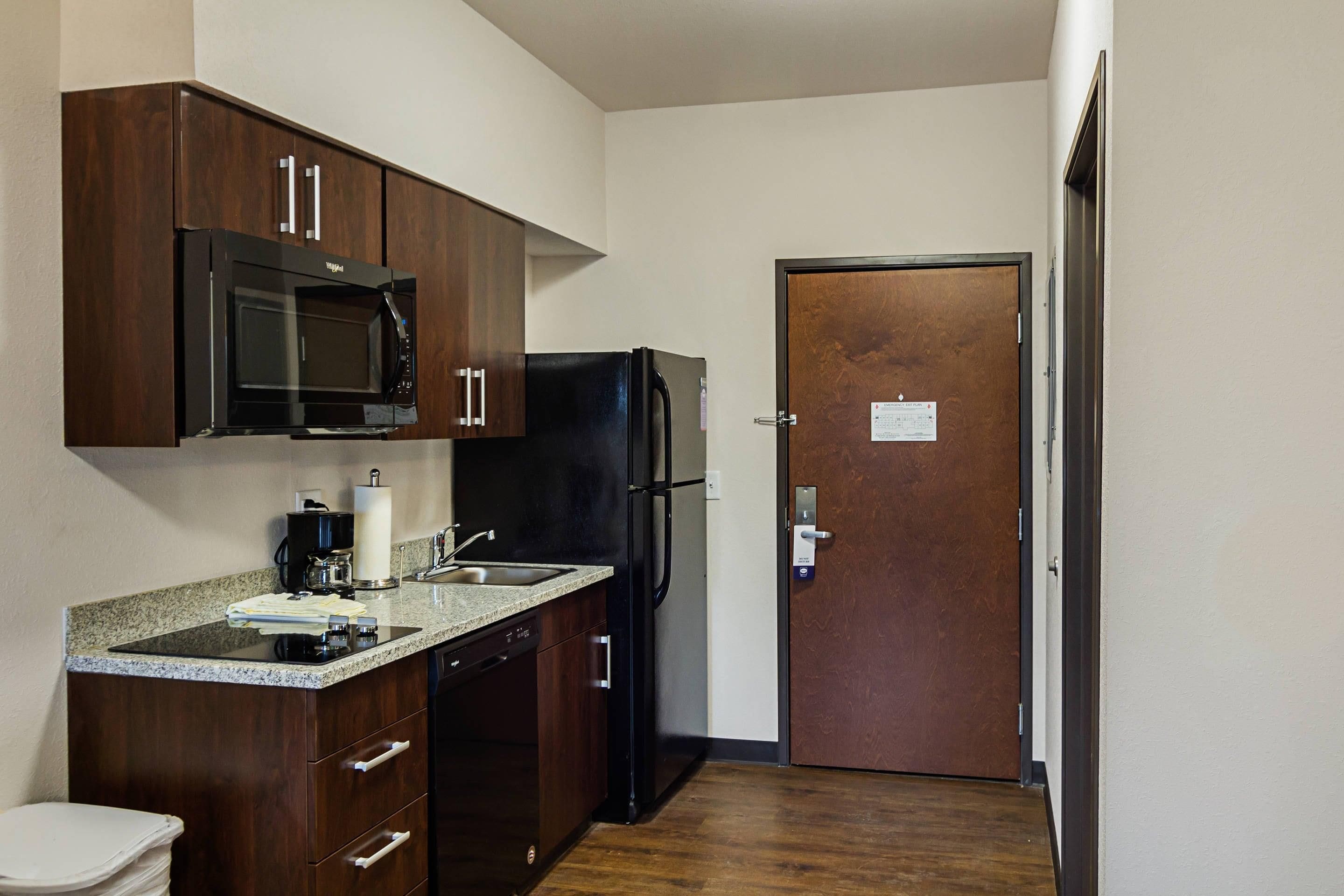 A compact kitchen with dark wood cabinets, a black microwave, a refrigerator, and a sink with a faucet.