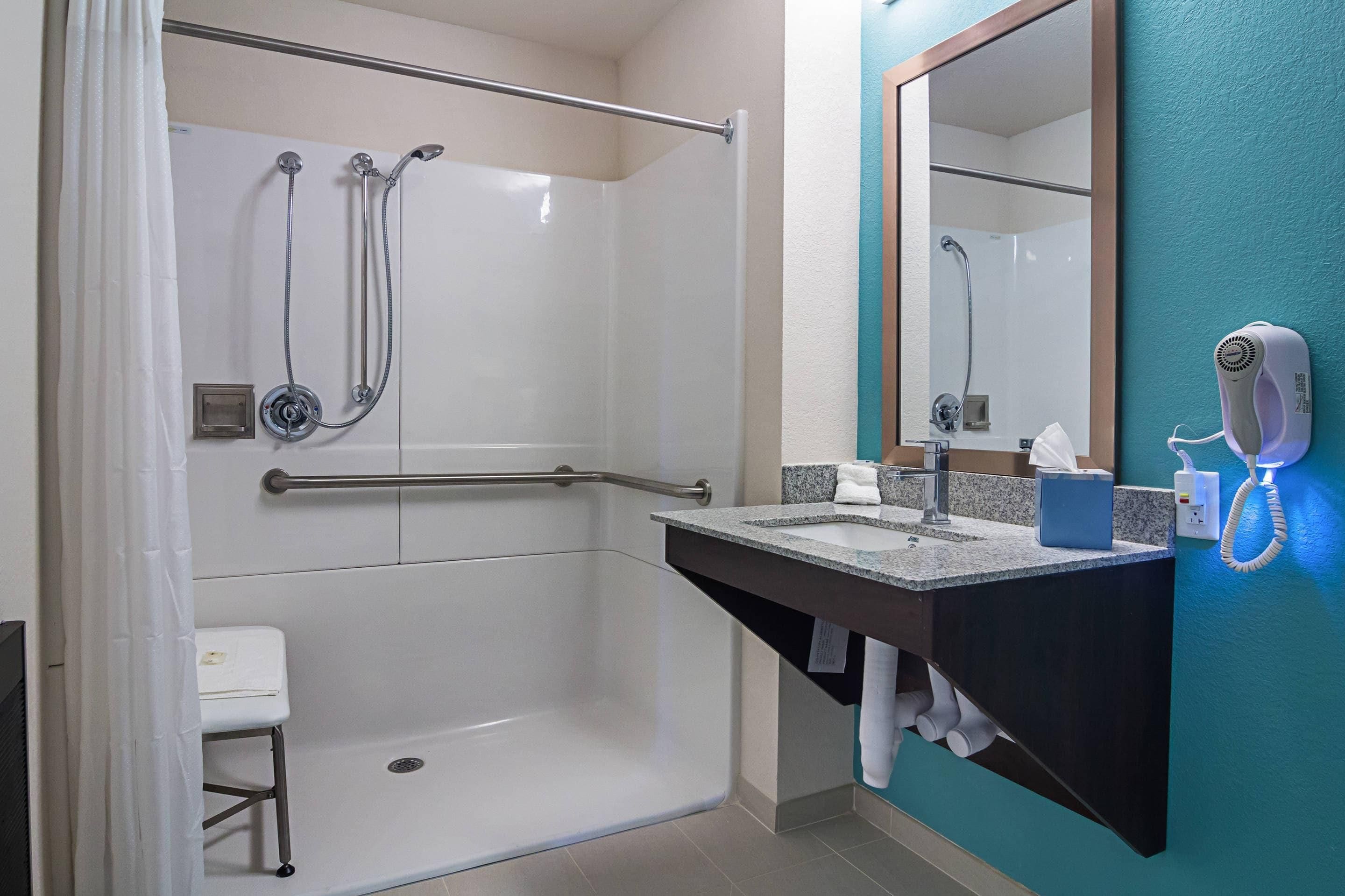 A modern bathroom with a walk-in shower, a vanity with a mirror, and a hairdryer mounted on the wall.