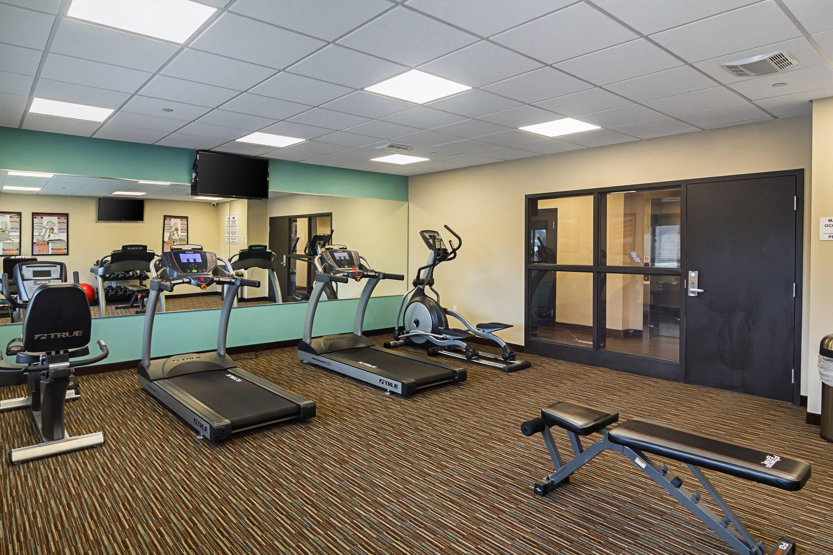 A fitness center with treadmills, elliptical machines, and a bench.