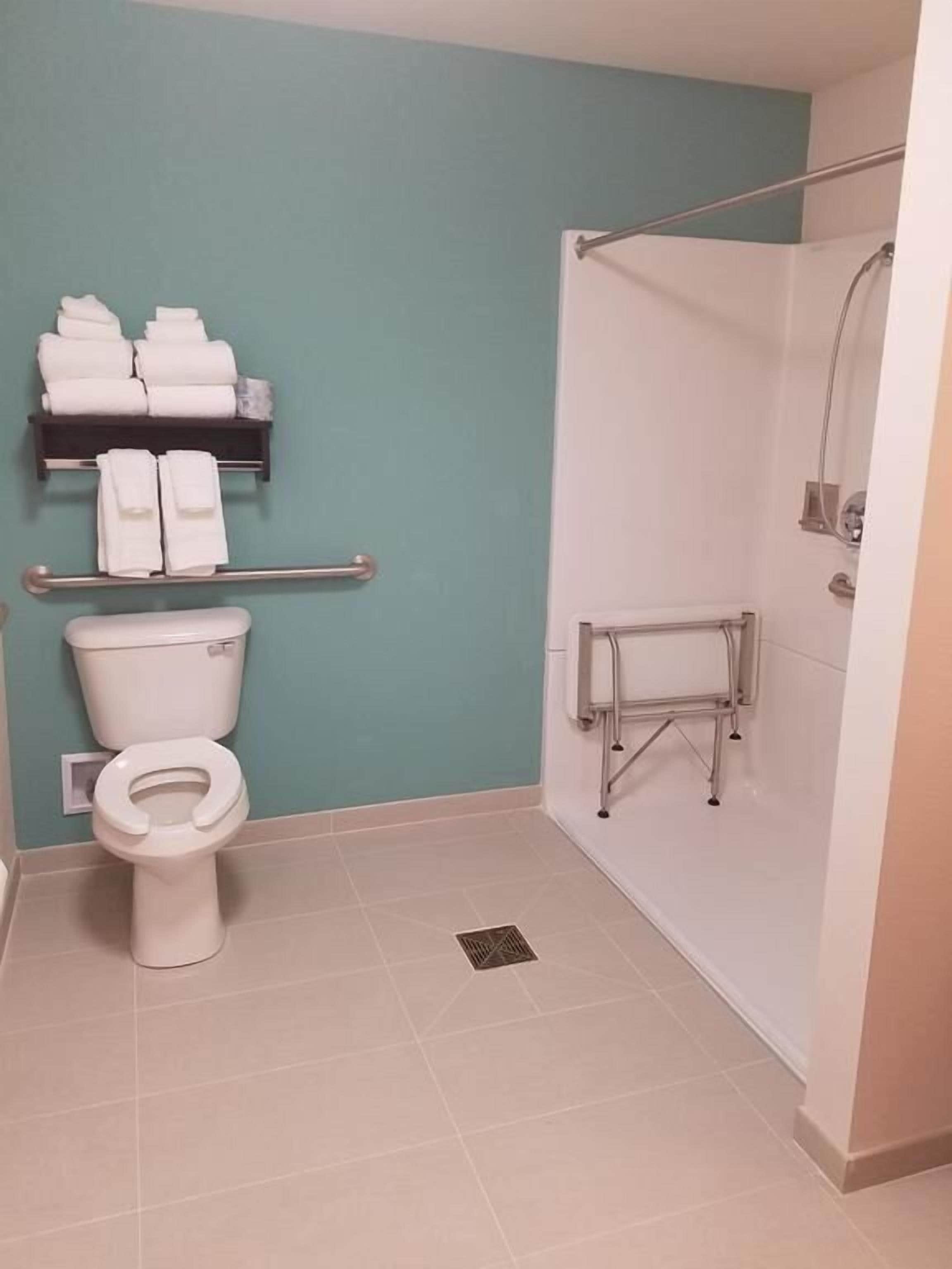 Un baño con inodoro, estante con toallas y zona de ducha.