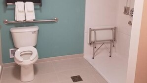 A bathroom with a toilet, a shelf with towels, and a shower area. - Suburban Studios Monaca - Pittsburgh (Monaca)