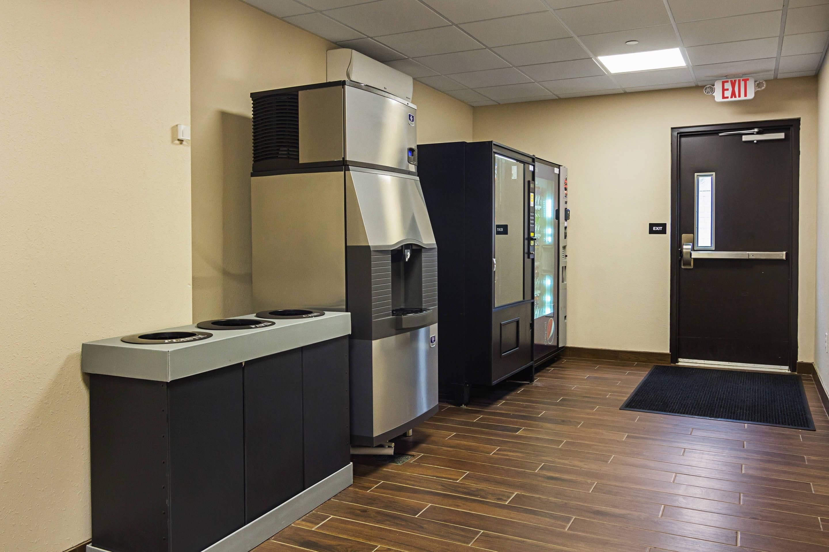 A hallway with a trash bin, a vending machine, and an exit door.