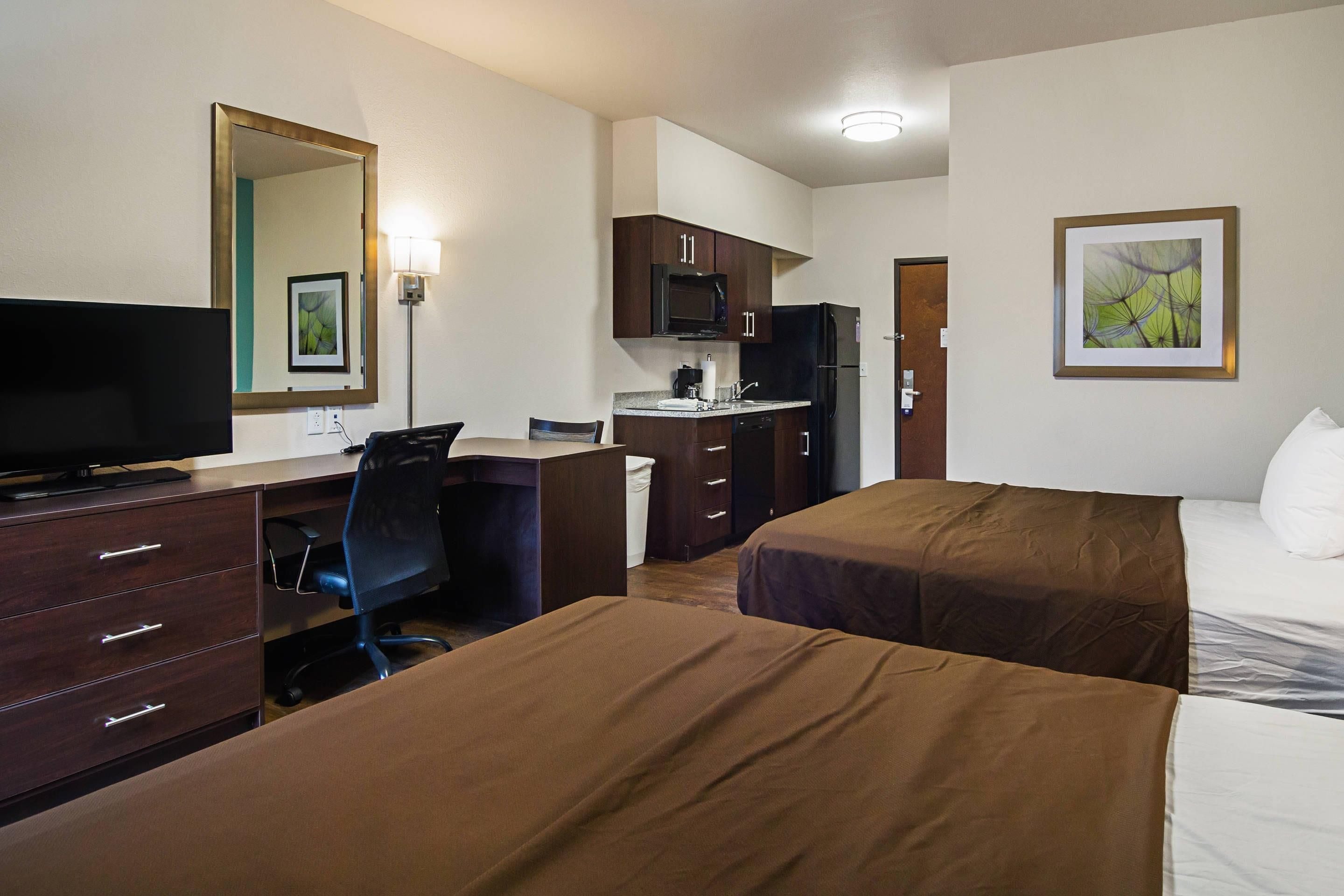 Habitación de hotel con cama, escritorio con silla, televisor, microondas y una pequeña kitchenette.