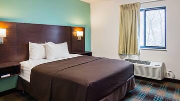 Quarto de hotel com cama, mesa de cabeceira, luminária na parede, janela com cortinas e ar condicionado.