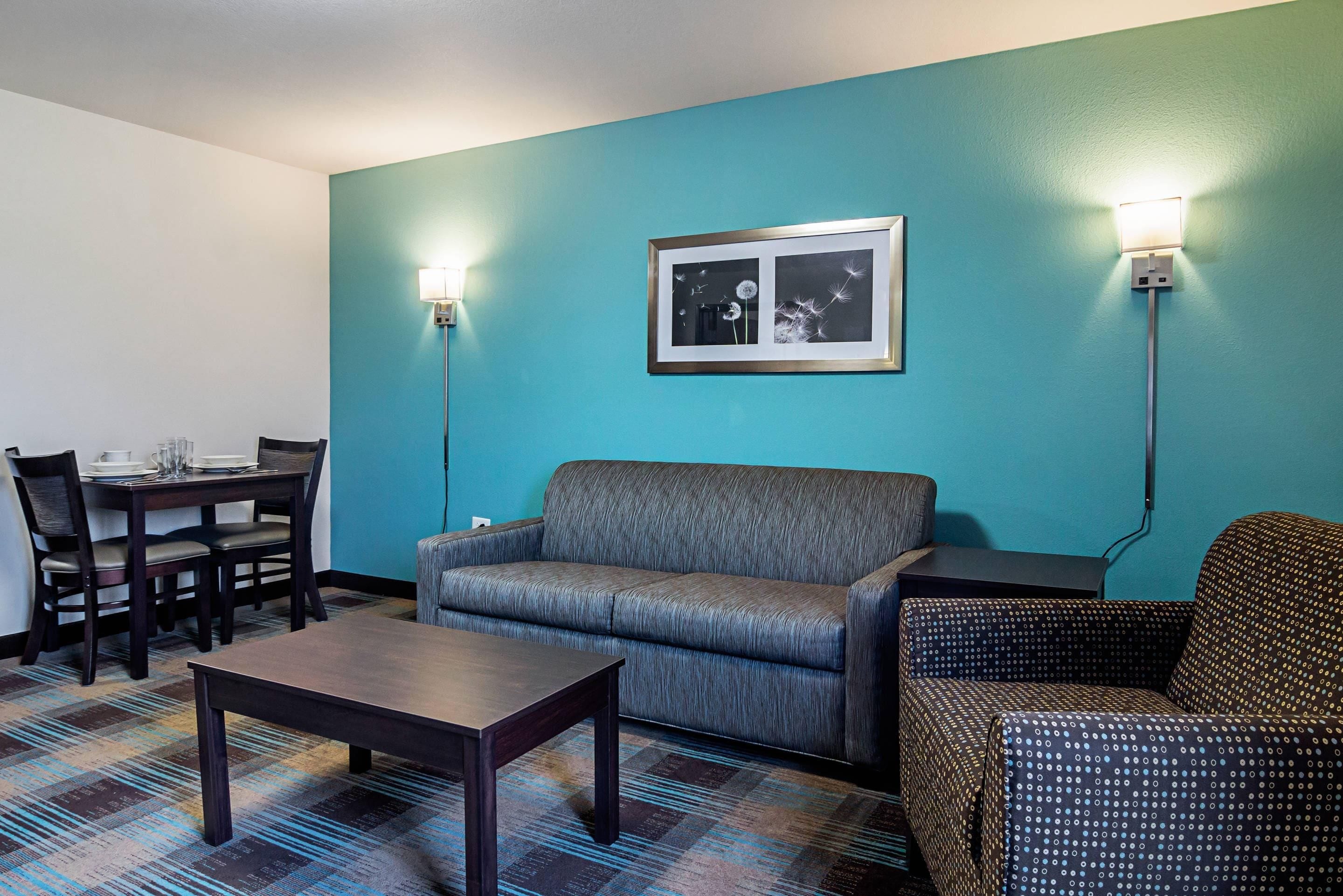 Una habitación con pared verde azulado, un cuadro enmarcado, un sofá, una mesa de comedor con sillas y una alfombra estampada.
