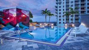 A swimming pool with lounge chairs and palm trees, surrounded by a modern building with a geometric facade. - Circ Hotel (Hollywood)
