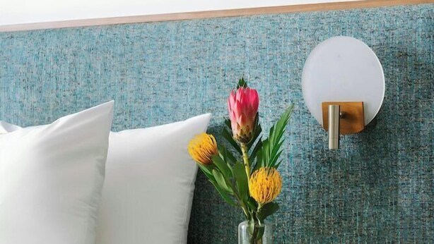 A hotel room with a bed, a nightstand, a vase with flowers, and a wall-mounted light fixture. - Circ Hotel (Hollywood)